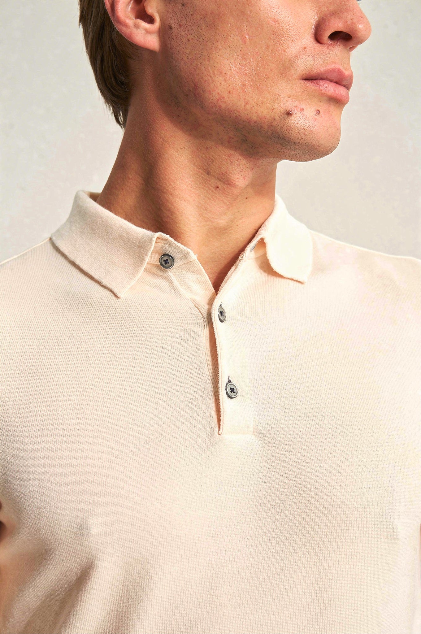 Close-up of a person wearing a beige polo shirt with a plain background